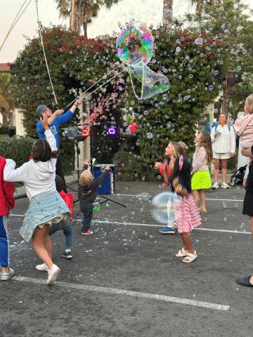 Children joyfully chasing and popping colorful soap bubbles in an outdoor park setting during a lively event.